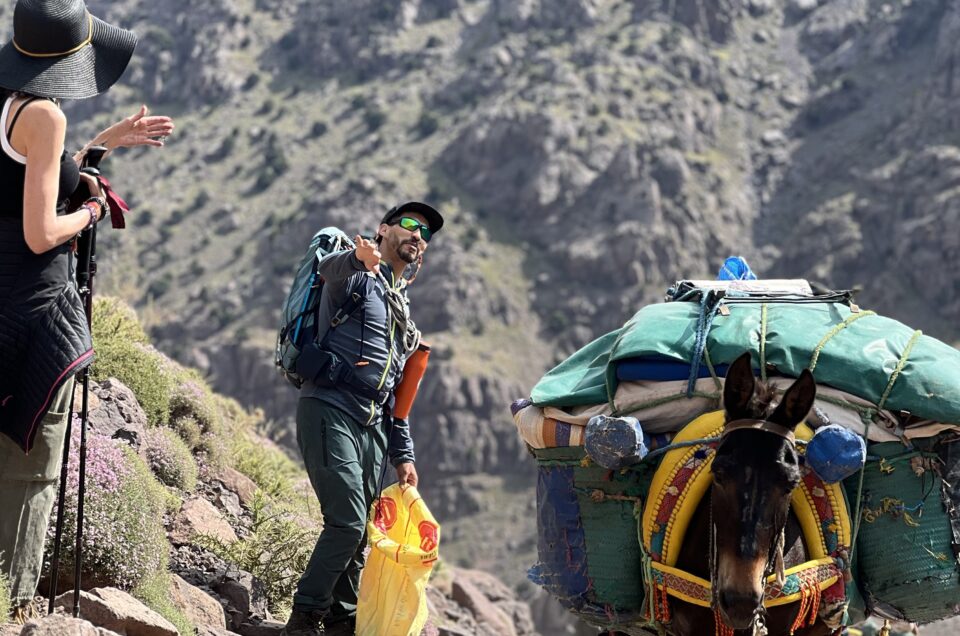 Guide explaining to hikers why it's safer to stand on the mountain side when passing a mule on a narrow trail in the Atlas Mountains